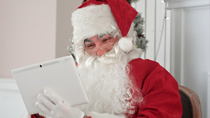 Joyful Santa Claus checking up Christmas emails from children on his digital tablet