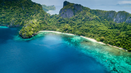 Drone view of a beautiful deserted tropical island with jungle, cliffs and fringed by coral reef © whitcomberd