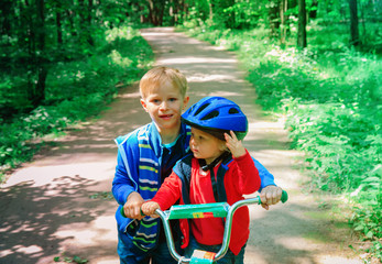 Obraz premium big brother helping little sister to ride bike in nature