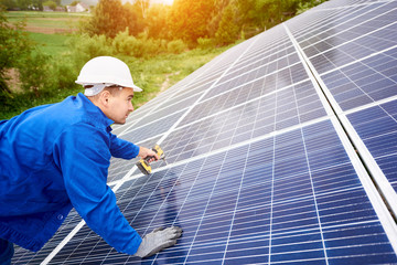 Construction worker connects photo voltaic panel to solar system using screwdriver. Professional installing and construction of solar system, alternative energy and financial investment concept.