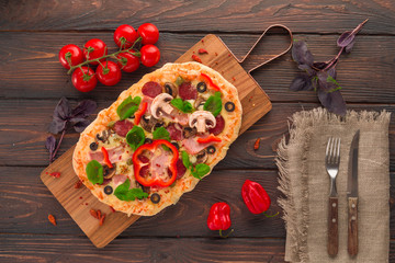 Homemade pizza with ham, pepperoni, mushrooms, capers and olives on a dark wooden table.