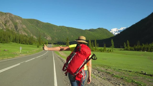 The woman the traveler, with a red backpack, goes along the road. Mountain area.
