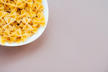 Raw farfalle pasta in bowl isolated on white background. Flatlay style, top view. Traditional italian cuisine.
