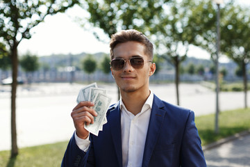 Handsome young businessman walks with dollar cash along the street