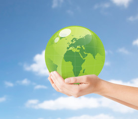 earth day, people, ecology and environment concept - close up of female hands holding green globe over blue sky and clouds background