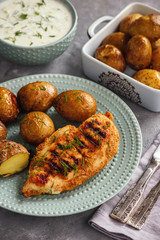 Grilled chicken fillet with baked potatoes and garlic yogurt dip.