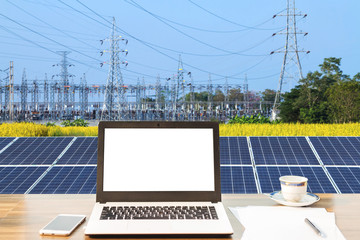 Mockup image of laptop with blank white screen,smartphone,coffee cup on wooden table of solar panel on high voltage tower in blue sky background, Alternative energy concept,Clean energy,Green energy.