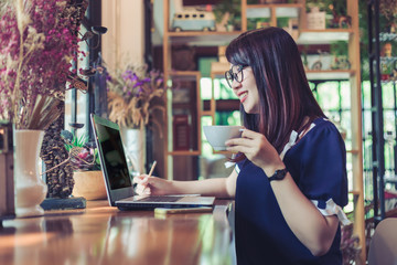 Asian business female working with laptop make a note in coffee shop like the background.