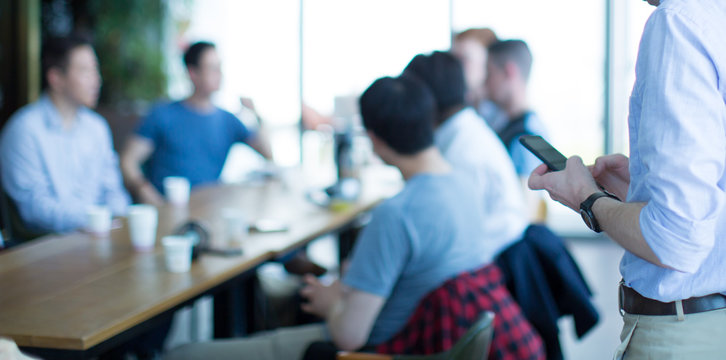 Man in Casual Clothes Looking at Phone During Business Meeting. Blurred Bokeh Defocused Group of People Meeting Seminar. Team Building Conference Support People.