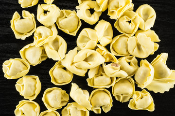 Fototapeta na wymiar Tortellini raw pasta flatlay on black wood background Italian traditional dumpling.