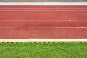 Fototapeta premium White lines of stadium and texture of running racetrack red rubber racetracks in outdoor stadium are 8 track and green grass field,empty athletics stadium with track.