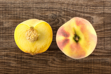 One yellow peach and a half with a drupe flatlay on brown wood background.