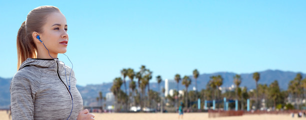 fitness, sport and technology concept - happy woman running and listening to music in earphones over venice beach background in california