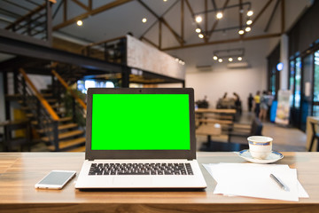 Mockup image of laptop with blank green screen on wooden table of In the coffee shop.  