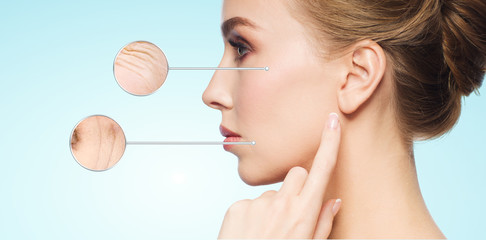 beauty, anti-aging and and people concept - beautiful young woman touching her skin over blue background