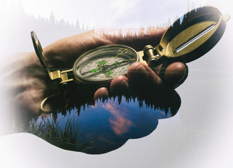 Man's hand with a compass. Double exposure, beautiful landscape background. Made in vintage style.