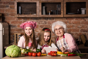Granddaughter and grandmother with tablet searching recipe to cook healthy vegetarian salad