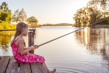 Ein Schulmädchen sitzt auf dem Steg an einem See und angelt