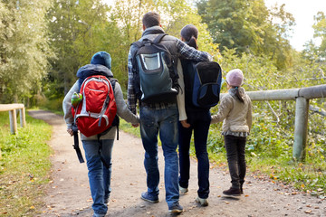 family, tourism and hiking concept - happy mother, father, son and daughter with backpacks walking...