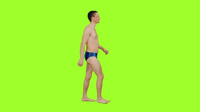 Young male in swim trunks walks on green screen background, Chroma key