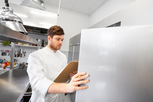 Cooking, Profession And People Concept - Male Chef Cook With Clipboard Doing Inventory And Looking To Fridge At Restaurant Kitchen