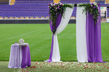 The decorative arch of violet color, for a ceremony of a solemn wedding is installed on the football field of stadium.