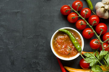 Hot chili peppers multi-colored, tomato cherry on branch, garlic and other spices on black background Copy space
