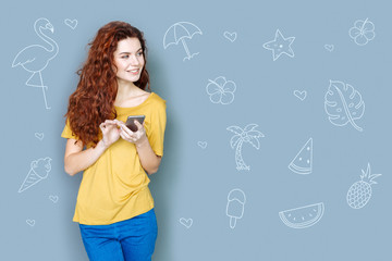 Planning the journey. Cheerful emotional student standing with a smartphone in her hands and smiling while planning her summer holidays