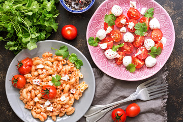 Mozzarella with tomatoes and pasta with sauce and cheese on a dark background. Italian food. View from above