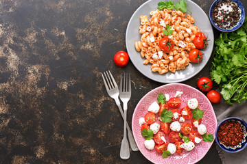 Macaroni with sauce, salad with tomato and mozzarella cheese. A view from above, a copy of the space.