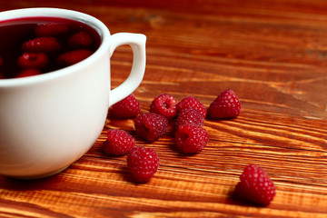 Tea with raspberries and berries next to a cup, on a wooden vintage table.
