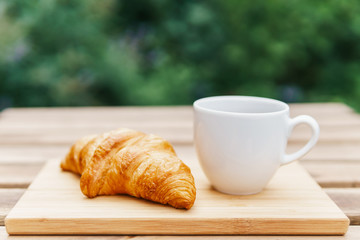 White Coffee Cup And French Croissant On Wooden Table In Green Garden