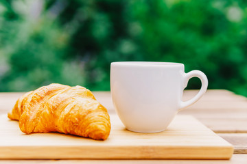 White Coffee Cup And French Croissant On Wooden Table In Green Garden