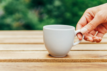 Woman Hand Raising A Cup Of Coffee From Wooden Table In Garden