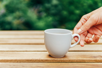 Woman Hand Raising A Cup Of Coffee From Wooden Table In Garden