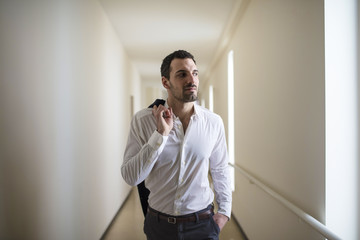 successful man walks with jacket on shoulder, office corridor