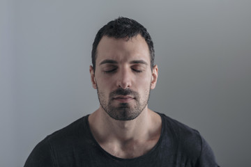 close portrait of young handsome man on neutral background, focused on his thoughts, with his eyes closed