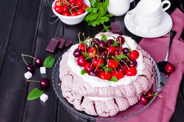 Chocolate Pavlova cake with whipped cream and cherries on a black wooden background