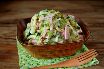 Salad with sausage, cabbage and cucumber in a wooden bowl