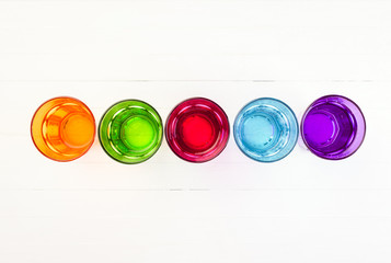 Multicolored glass glasses on a white background, top view, copy space
