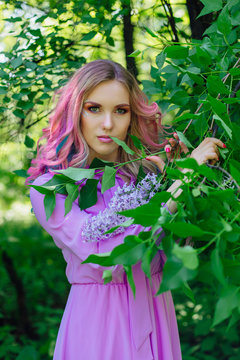 Beautiful girl with colorful dyed hair and perfect makeup and hairstyle standig next to lilac bush