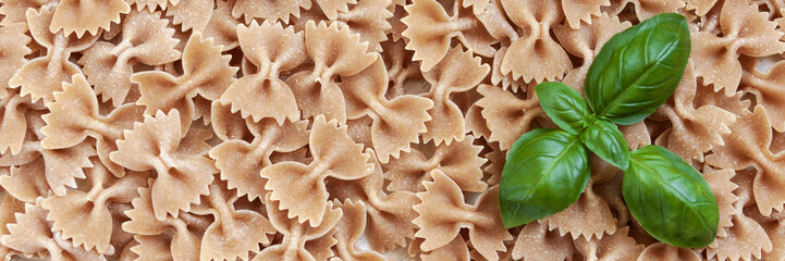 Panoramic background with spilled raw pasta farfalle and fresh basil