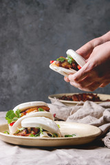 Man's hands hold asian sandwich steamed gua bao buns with pork belly, greens and vegetables served...