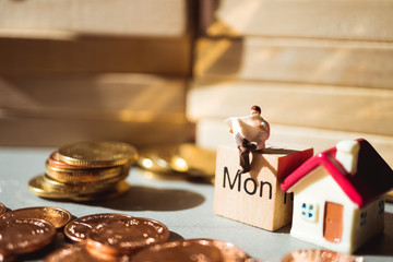 Miniature people, man reading on monday wooden block and stack coins using as business concept