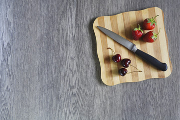 Cherries, strawberries and knife on cutting Board on wooden table 
