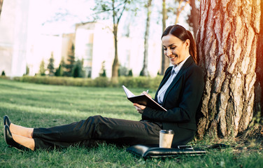Attractive smiling business woman in suit something writes down in a paper notebook sitting under a...