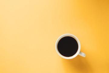 Hot black coffee in white cup on yellow background
