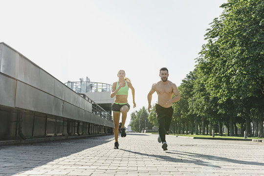Pretty sporty woman and man jogging at city