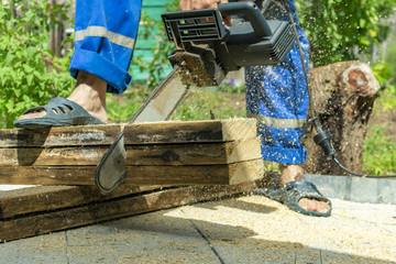 a man in blue work clothes cuts pine boards electric with a hand saw, standing in slippers