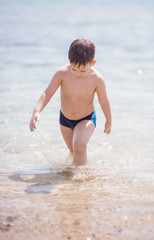 Adorable boy standing in the water on the beach. Family vacation or holiday concept.